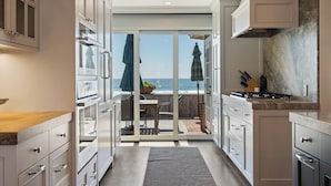 A modern kitchen with white cabinetry, a gas stove, and a view of the ocean through a sliding glass door.