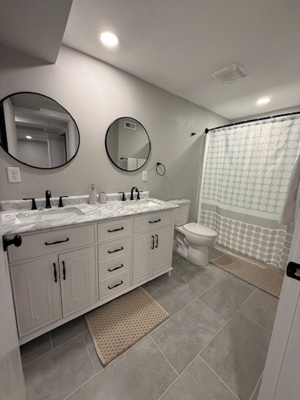 Een moderne badkamer met een witte wastafel, twee ronde spiegels, een toilet en een douche met een stippen gordijn.