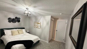 Un dormitori amb un llit, un ventilador de sostre, una porta i un mirall fixat a la paret.