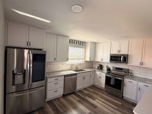 A modern kitchen with white cabinets, stainless steel appliances, and a wooden floor. - Family friendly home just 15 minutes from the Events Center, airport, & downtown (Casper)