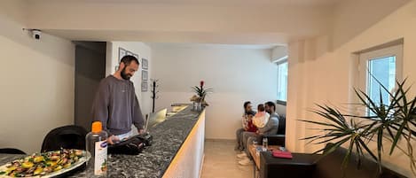 En modern hotellobby med en marmordisk i receptionen, en sittgrupp med en soffa och ett soffbord samt en krukväxt.