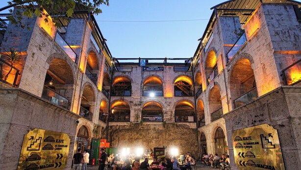 An outdoor dining area with stone arches and a brick wall, featuring signs for Kafe and Balibet Han. - Zeus Suit Görükle (Bursa)
