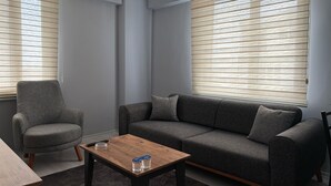 A modern living room with a grey sofa, a matching armchair, and a wooden coffee table. - Zeus Suit Görükle (Bursa)