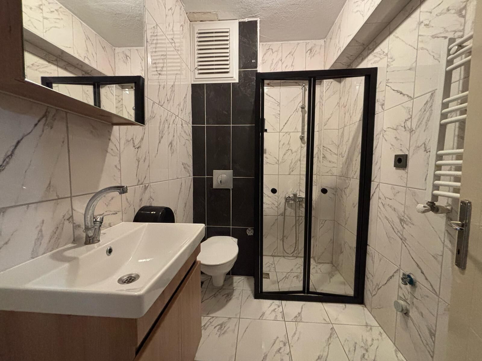 A bathroom with a marble-tiled floor, a white sink, a toilet, and a glass-enclosed shower area.