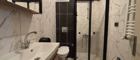 A bathroom with a marble-tiled floor, a white sink, a toilet, and a glass-enclosed shower area.