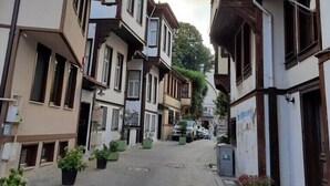 A narrow street lined with traditional buildings, featuring balconies and potted plants. - Zeus Suit Görükle (Bursa)