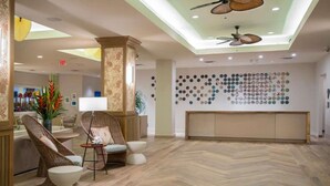Un hall d’entrée doté d’un parquet en chevrons, de fauteuils en osier, d’un comptoir de réception et d’un mur recouvert de miroirs ronds.