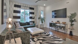 Ein modernes Wohnzimmer mit einem grünen Sofa, einem weißen Hocker, einem Zebra-Muster-Teppich, einem Fernseher und einem Deckenventilator.