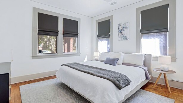A bedroom with a bed, a ceiling fan, and two windows with dark blinds.