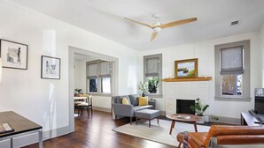 A spacious living room with hardwood flooring, a ceiling fan, a fireplace, and a dining area with a table and chairs.