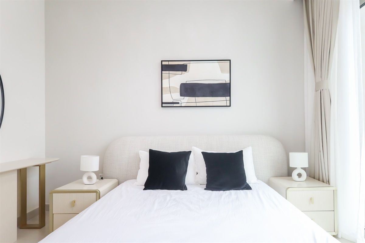 Une chambre d’hôtel avec un lit, deux tables de chevet, une œuvre d’art accrochée au mur et une fenêtre avec des rideaux.