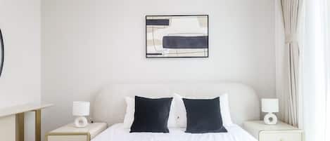 Una habitación de hotel con una cama, dos mesitas de noche, un cuadro colgado en la pared y una ventana con cortinas.