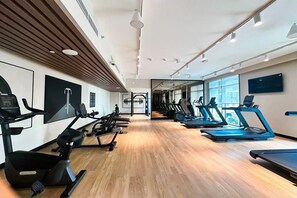 Ein Fitnessraum mit Trainingsgeräten, Holzboden und großen Fenstern.