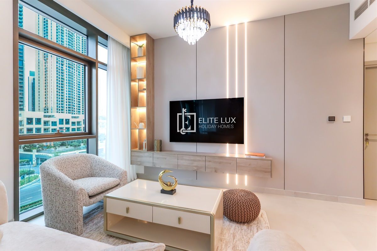 A modern living room with a large window, a flat-screen TV, and a chandelier.