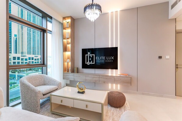 A modern living room with a large window, a flat-screen TV, and a chandelier.