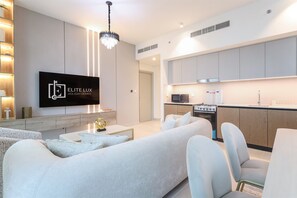 Ein modernes Wohnzimmer mit Flachbildfernseher, einer Couch und einem Essbereich, im Hintergrund befindet sich eine Küche.
