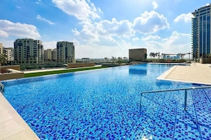 A swimming pool with a tiled edge, surrounded by buildings and a clear sky.