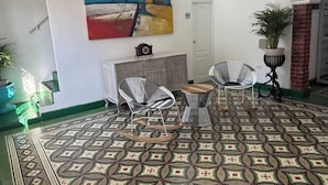 A room with a patterned floor, two rocking chairs, a small table, a clock, and a colorful abstract painting on the wall. - Turbay House 10 (Cartagena de Indias)