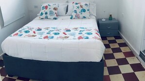 A bedroom with a checkered floor, a bed with a white duvet and patterned pillows, a bedside table with a lamp, and a window with a view. - Turbay House 12 (Cartagena de Indias)