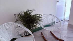 Two white wicker rocking chairs with wooden bases, positioned on a tiled floor with a potted plant nearby. - Turbay House 4 (Cartagena de Indias)