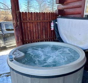 Un bain à remous en plein air, entouré d’une clôture en bois, avec un véhicule visible au loin.