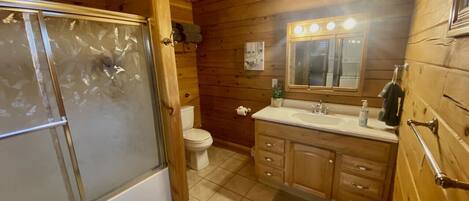A wooden cabin bathroom with a glass shower enclosure, a toilet, a sink with a mirror, and wooden cabinets.