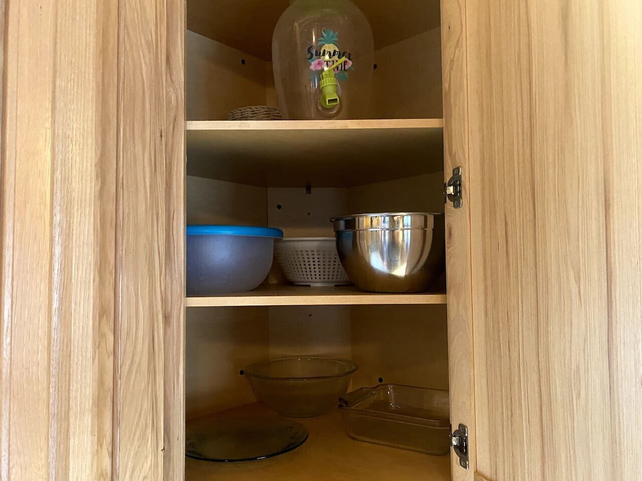 Un armario de madera con estantes que contiene utensilios de cocina, incluyendo un tazón azul, un bol de acero inoxidable y un tazón de vidrio transparente.