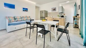 A modern living room with a sofa, dining table, and chairs. There is a kitchen area with cabinets and a refrigerator. - Sea Life Giulia, 200 meters from the beach (ALCAMO)