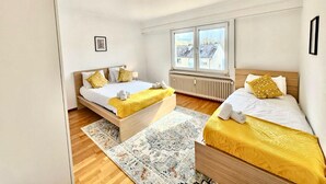 A modern bedroom with two beds, a large window, and a radiator. - Charming 3 bedrooms with a cozy terrace (Walferdange)