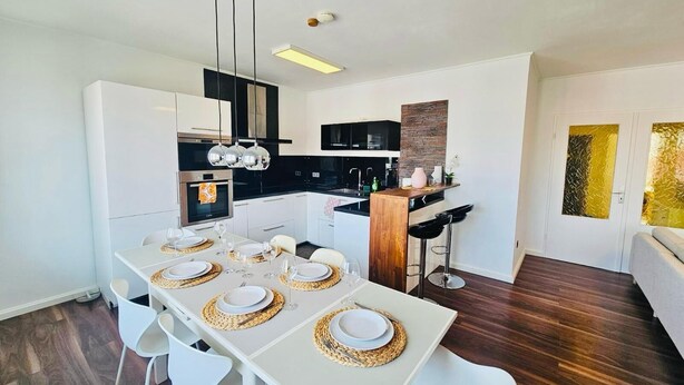 A modern kitchen with white cabinets, a black countertop, and a wooden island. - Charming 3 bedrooms with a cozy terrace (Walferdange)