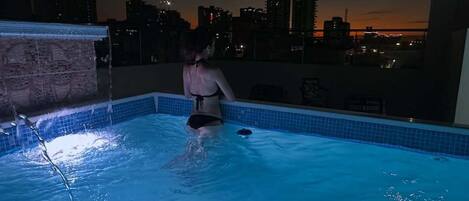 A person in a swimming pool at night with a cityscape in the background.