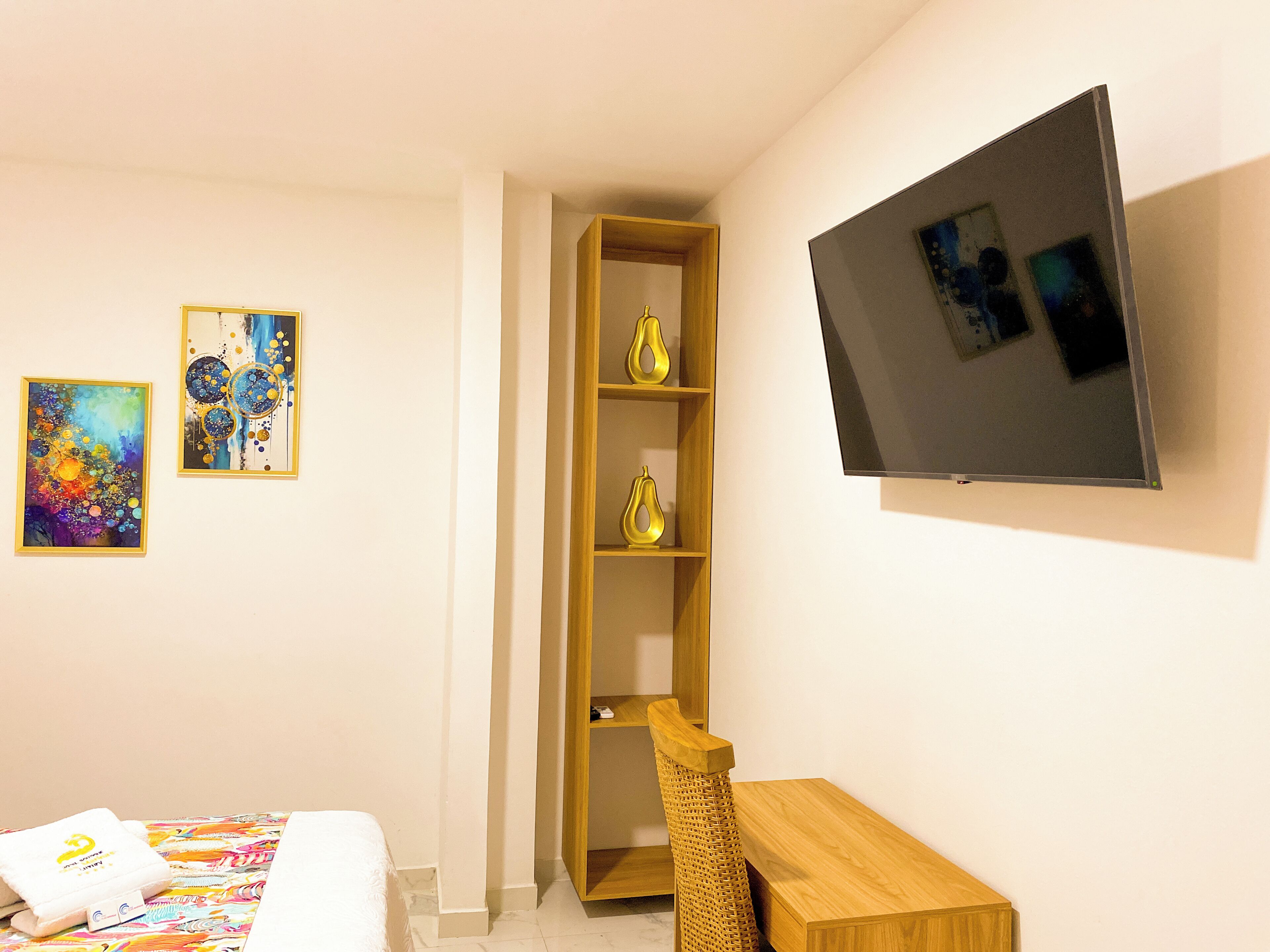 Una habitación de hotel con una cama, un escritorio, un televisor y dos cuadros.
