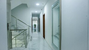 Un pasillo limpio y moderno con una escalera de cristal y una puerta que da a otra habitación.