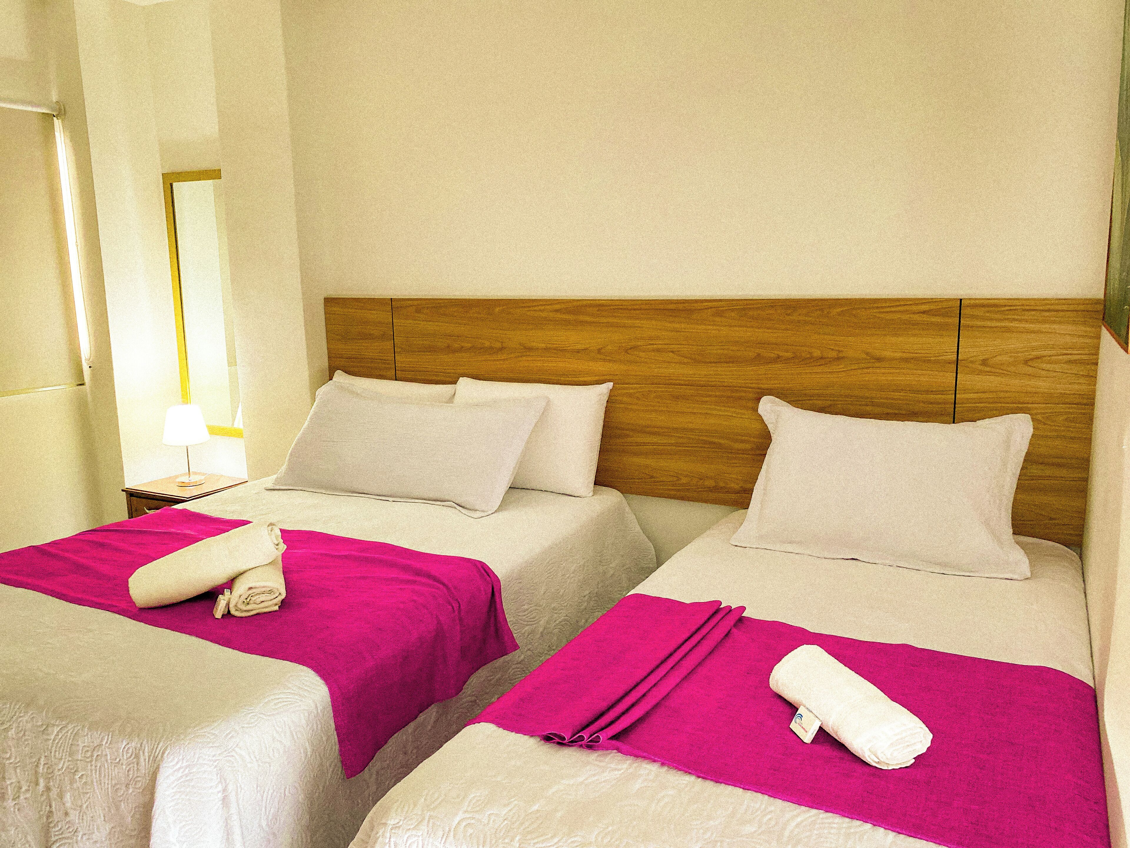 Dos camas individuales con cabeceros de madera, ropa de cama blanca y toallas rosas.