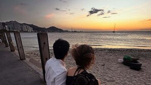 Una pareja sentada en un camino de concreto al borde del mar durante el atardecer.