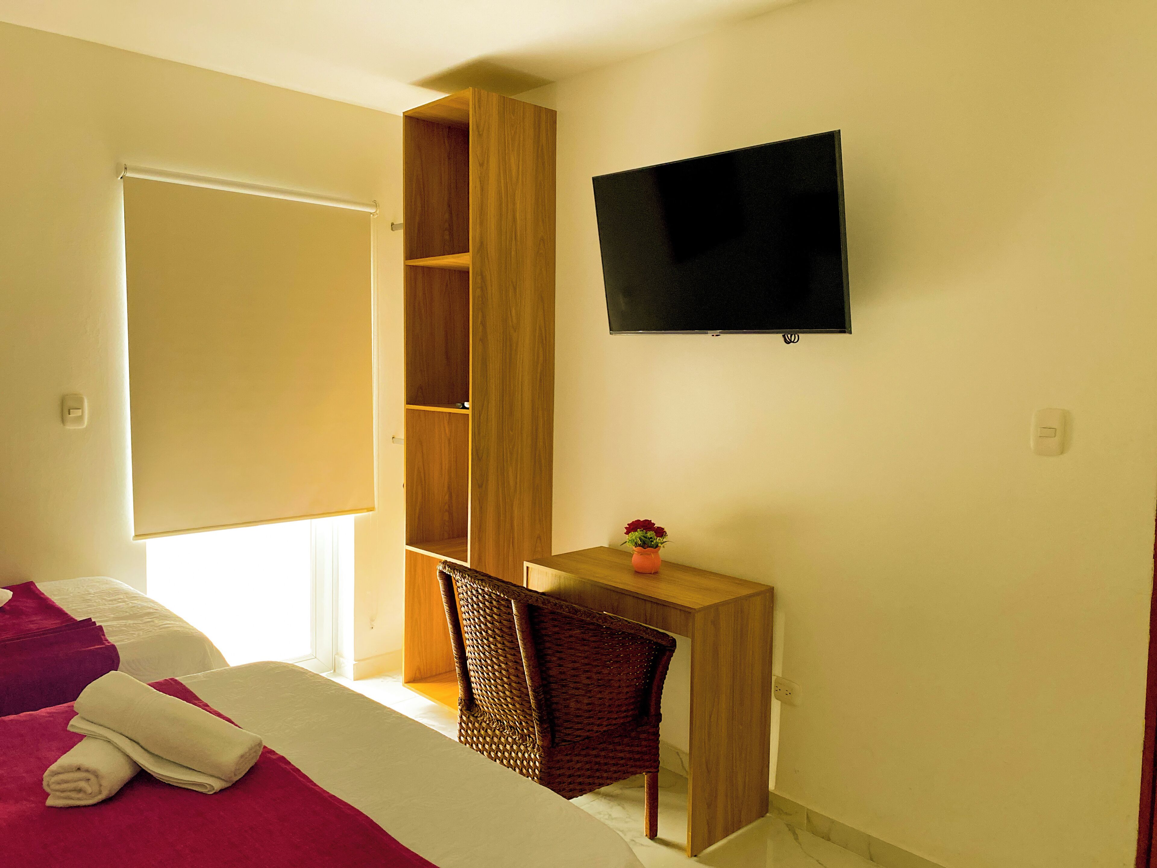 A hotel room with a bed, a desk, a chair, a TV, and a wardrobe.