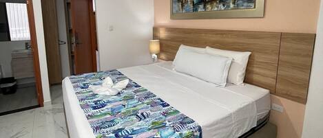 A hotel room with a bed, a painting of boats on the wall, a nightstand, and a bathroom visible in the background.