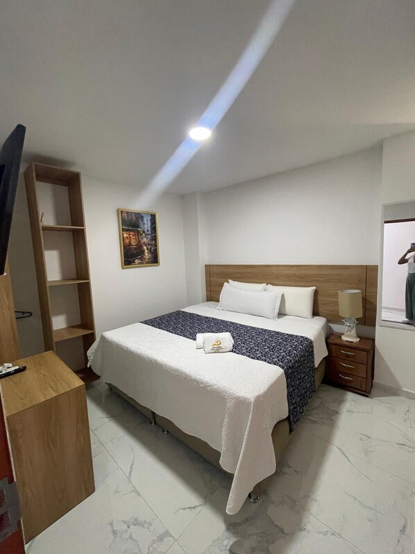 A hotel room with a bed, a wooden nightstand, a night lamp, a painting on the wall, and a wooden wardrobe. - HOTEL BOUTIQUE OLAS MARINAS LUXURY (Santa Marta)