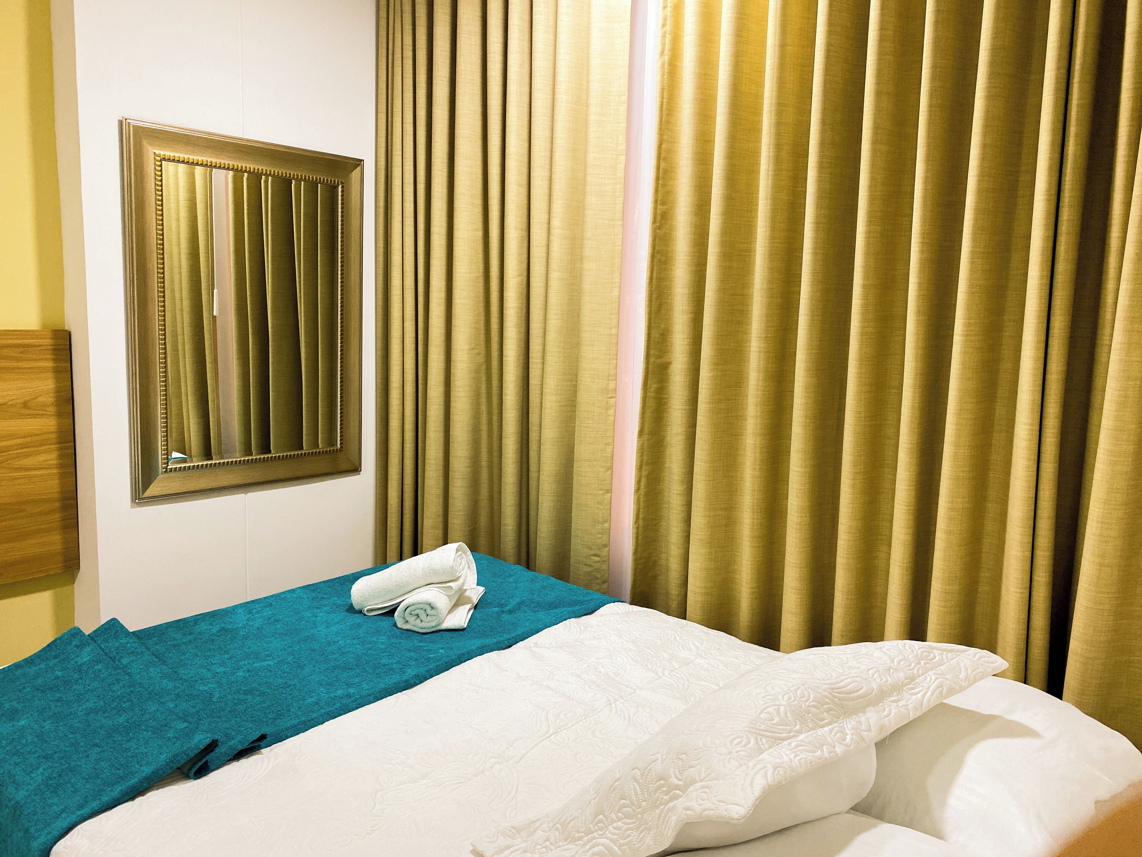 A hotel room with a bed, a mirror, and curtains.