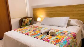 A neatly made bed with a colorful bedspread, a white pillow, and a rolled towel.