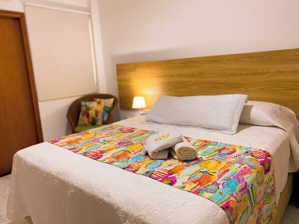 A neatly made bed with a colorful bedspread, a white pillow, and a rolled towel. - HOTEL BOUTIQUE OLAS MARINAS LUXURY (Santa Marta)
