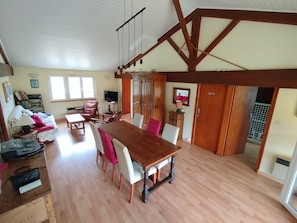 A spacious living area with a wooden dining table, chairs, a sofa, and a television.
