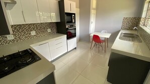 Een moderne keuken met witte kastjes, een gasfornuis, een magnetron en een oven. Er is een eettafel met een rode stoel en een raam met uitzicht.