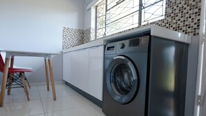 Een praktische keuken met een ingebouwde wasmachine, een eettafel met stoelen en een raam met uitzicht.