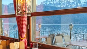 A dining area with a table set for four, overlooking a lake with mountains in the background. - Seehotel Schwert (Gersau)
