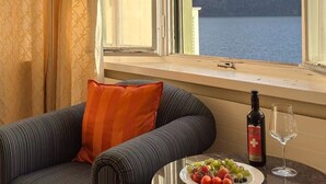 A room with a sofa, a table with a bottle and glass, and a window with a mountain view. - Seehotel Schwert (Gersau)