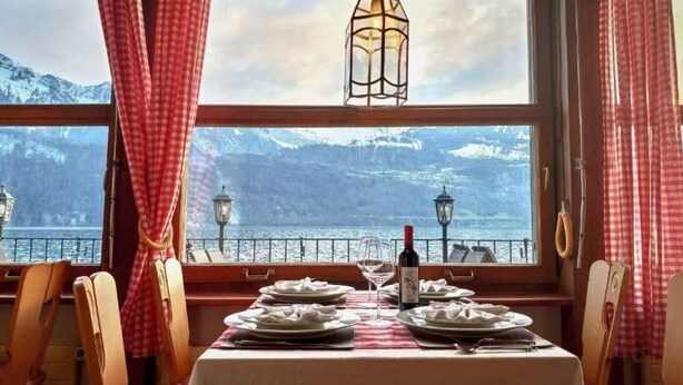 A dining table set with plates, a wine bottle, and glasses, overlooking a mountainous landscape with a body of water. - Seehotel Schwert (Gersau)