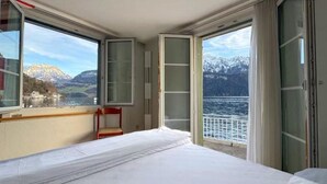 A room with a bed, a chair, and a large window offering a view of a lake and mountains. - Seehotel Schwert (Gersau)