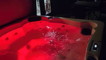 A hot tub with a red light, a wooden bench, and a view of the outside.