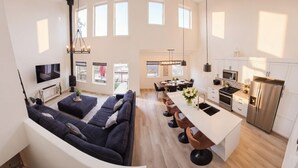 A modern open-plan living area with a sofa, dining table, kitchen, and large windows.
